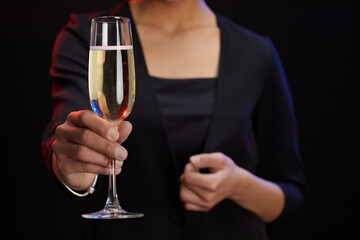 Mid section portrait of unrecognizable elegant woman holding champagne glass while standing against black background at party, copy space