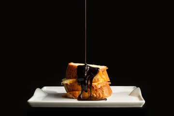 Bizcocho con chocolate derretido cayendo por arriba sobre un plato blanco y un fondo negro. Vista de frente y de cerca. Copy space
