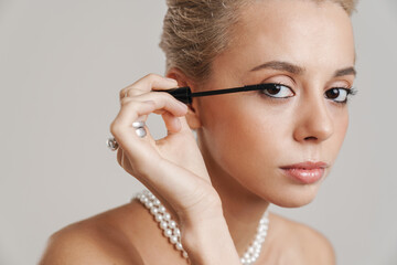 Sensual shirtless girl wearing necklace applying mascara