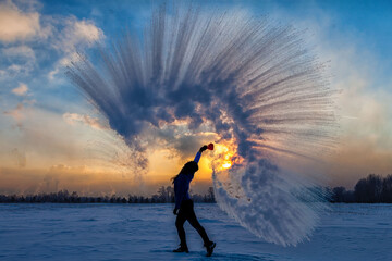 Silhouette of a sports girl at sunset in winter. Woman splashed boiling water on cold air.