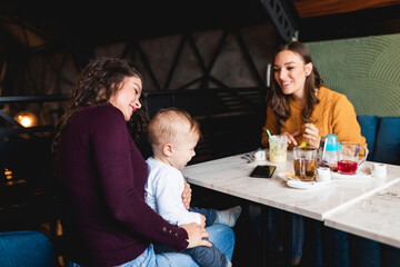 Two friends enjoying in cafe bar with cute little baby boy.