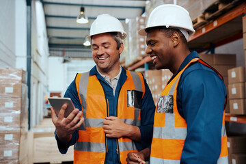 Multiethnic factory engineers smiling while looking at digital tablet screen at industrial warehouse