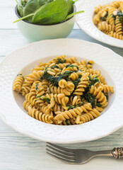 Whole grain fusilli pasta dish with spinach, pine nuts and lactose free cream sauce on white wooden table. Delicious vegan lunch.