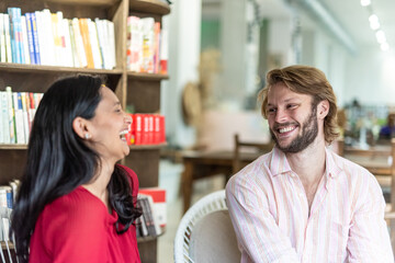 first date of a couple in love, focus on the blond Caucasian guy who smiles and looks at the Indian woman while laughing, meeting in a cafeteria and bookstore of two lovers, winking look of the man