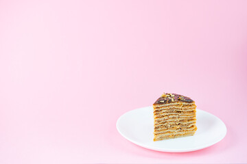 A slice of pancake cake with chocolate caramel and walnuts on a pink background. Maslenitsa or Shrovetide. Horizontal orientation, copy space.