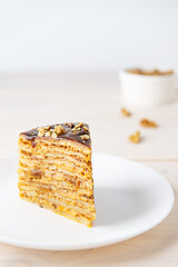 A slice of homemade pancake cake with chocolate caramel, walnuts and honey on a wooden table. Maslenitsa or Shrovetide.