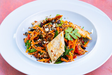 Delicious healthy Quinoa salad in a white plate isolated on a pink background close up.