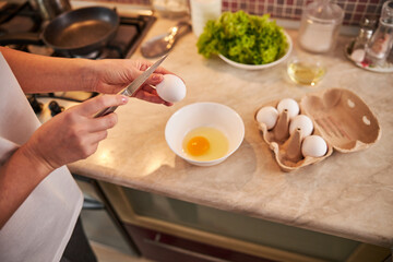 Sharpened knife is hanging over an egg