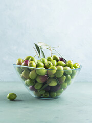 Freshly picked raw green olives in glass bowl on textured background.