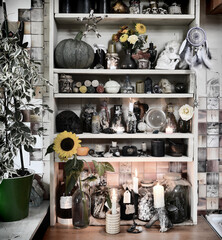 Desaturated still life with flowers, bottles, crystals, magic objects and burning candles on witch shelves.