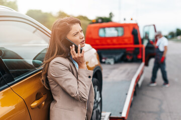 Elegant middle age business woman calling someone while towing service helping her on the road....