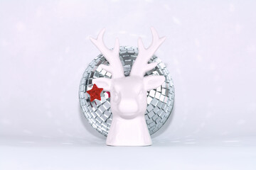 Christmas white porcelain deer with a red star on the ear on the background of a disco ball.