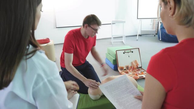CPR class with young caucasian instructors speaking and demonstrating help first aid, cpr mannequin on the floor.
