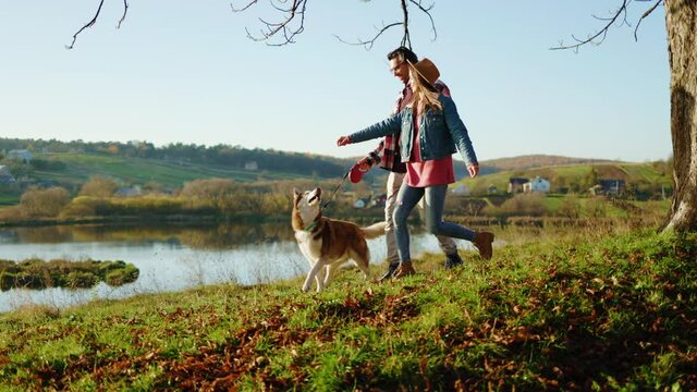 Man and woman lovely couple walking with domestic pet dog in autumn forest near lake. Animal relaxed portrait cheerful. Feel happy. At sunlight. Slow motion