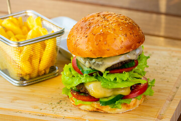 Delicious double beef burger with french fries in a metal basket on a wooden(bamboo) tray close up.