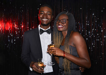 Waist up portrait of young African-American couple holding champagne glasses and smiling at camera while posing against sparkling background at party, shot with flash © Seventyfour