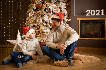 Father and son in christmas hats are enjoying near christmas tree in modern decorated home, Happy New year 2021