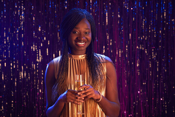 Waist up portrait of smiling African-American girl holding champagne glass and looking at camera while standing against sparkling background at party, copy space © Seventyfour