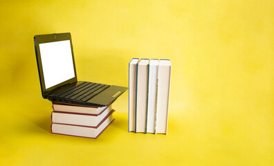 laptop and stack of books on yellow background