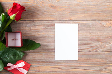 Valentines mockup with red rose and golden ring on the wooden background, flat lay with copy space, white card