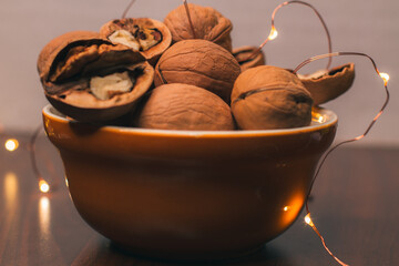 Whole walnut kernels in an orange ceramic bowl and crushed pecans. Christmas lights. Ingredients for cooking festive dishes. Close-up