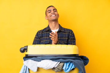 Traveler man with a suitcase full of clothes over isolated yellow background applauding