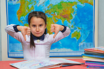 Portrait of a smart cute girl showing thumbs down on the background of the world map. The inscription on the map WORLD