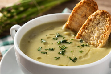 Fresh green asparagus soup in bowl on wooden table.Close up
