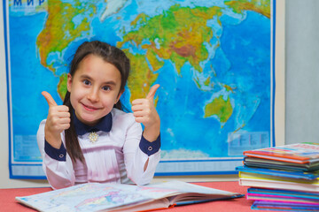 Portrait of a smart cute girl showing thumbs up on the background of the world map. The inscription on the map WORLD