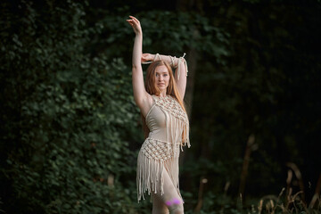 Portrait of a beautiful young graceful blonde woman dancing. In the woods in summer. Clothing of their eco-materials and macrame. The concept of natural products and harmony with nature.