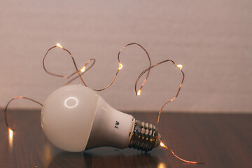 The concept of energy saving. White matte 7-watt energy-saving light bulb and Christmas lights on wooden table