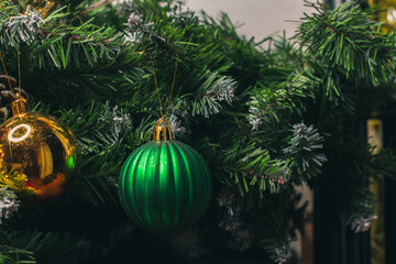 Green pine branches are decorated with green and gold Christmas balls. Home decoration for the New year. Christmas ornaments. Winter festivities