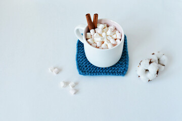 Dark blue handmade knitted coaster, natural cotton, cup with marshmallows and cinnamon over white