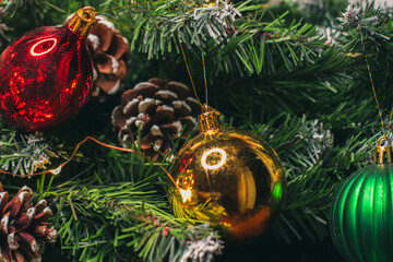 Christmas ornaments on the green branches of a fir tree. Pine cones, green, red and gold balls and yellow Christmas lights. Winter holiday. New year 2022