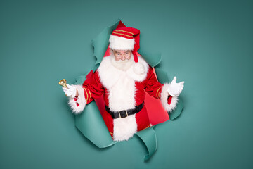 Surprised Santa Claus with a gold bell on a green studio background.