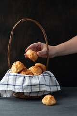 Basket with Traditional French Gougeres - savory cheese pastry and female hand taking one of the buns on dark background