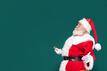 Surprised Santa Claus with a gold bell on a green studio background.