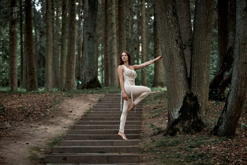 Beautiful young woman with long hair dancing in nature in summer on concrete steps. Clothing made of eco-friendly materials in beige and macrame.