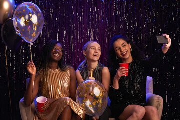 Portrait of three young women taking selfie photo at party while wearing sparkling dresses