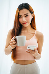 Beautiful young asian woman with a cup of coffee and smartphone.