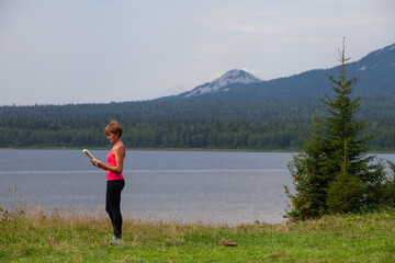 Obraz premium Young girl reads a book on the shore of a mountain lake