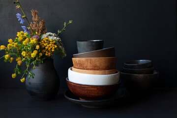 Still life with handmade ceramic dishware and field flowers in a black vase. Rustic style.