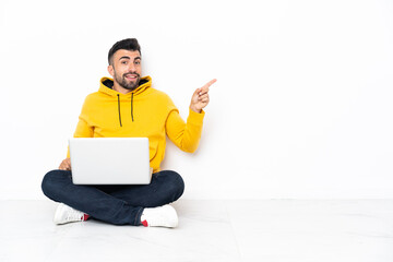 Caucasian man sitting on the floor with his laptop pointing finger to the side