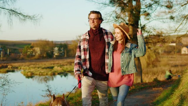 At sunlight man and woman lovely couple walking with domestic pet dog in autumn forest near lake. Animal relaxed portrait cheerful. Feel happy. Slow motion