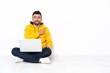 Caucasian man sitting on the floor with his laptop pointing to the side to present a product
