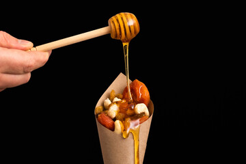 A man pours honey on dried fruit in a paper cone.