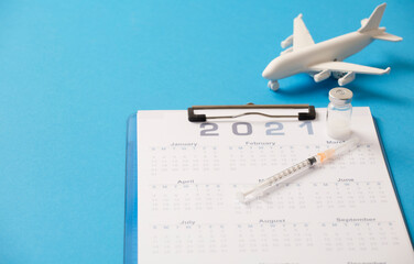 Syringe with vaccine canister, calendar 2021, and white plane, blue background