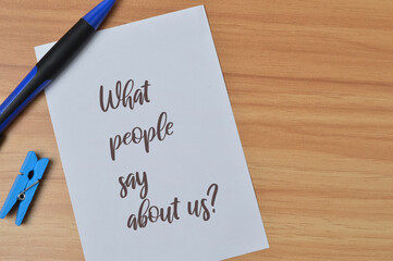 Top view of pen, clothespin and white paper written with question WHAT PEOPLE SAY ABOUT US?. Business and education concept.