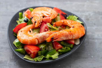 salad with fried shrimps on dark plate on ceramic background