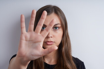 Portrait of a young serious woman in a black shirt, on a gray background, showing a stop symbol with her hand
